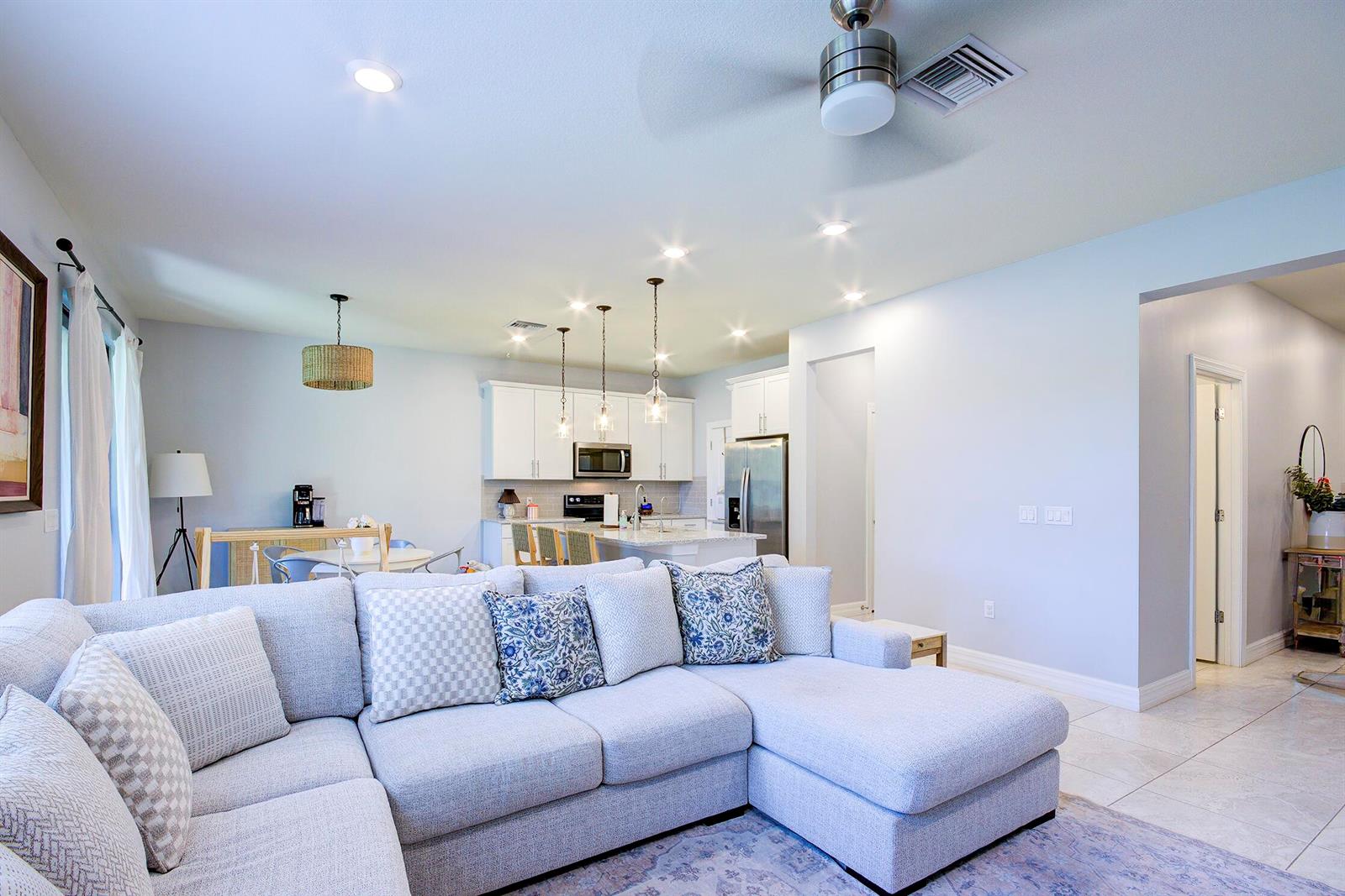 An open-concept living room features a light gray sectional sofa facing a white kitchen — 8327 Rearing Lane, Lake Worth FL 33467, LAKE WORTH, FL