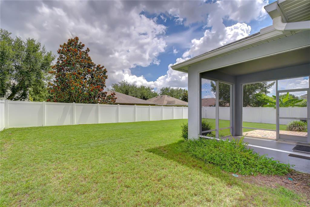 A grassy backyard features a white vinyl fence and a screened-in patio area — 426 SUMMERLYN DRIVE, VALRICO, FL