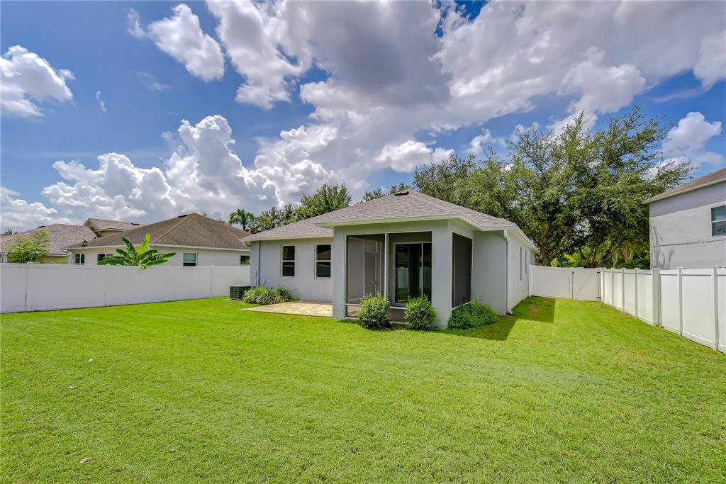 A backyard view of a single-story house with a screened-in patio and white vinyl fencing — 426 SUMMERLYN DRIVE, VALRICO, FL