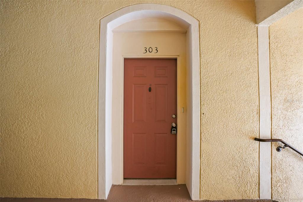 A red front door labeled 303 is set within a yellow stucco wall — 8775 SARTORI STREET UNIT 303, ORLANDO, FL