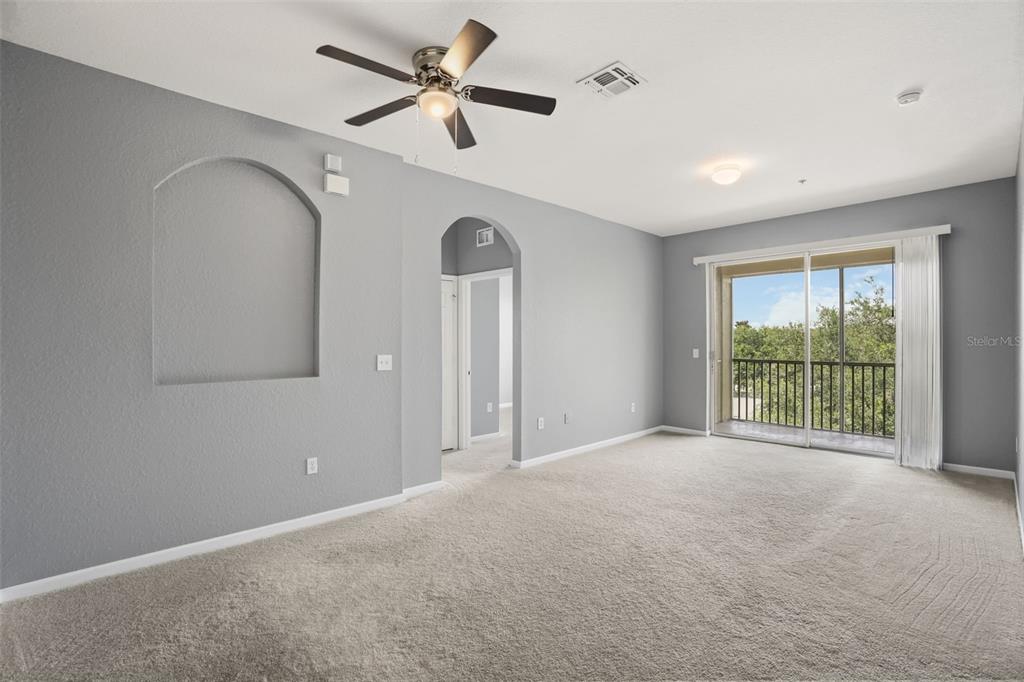 An empty living room features gray walls, beige carpeting, an arched wall niche, and a balcony — 8775 SARTORI STREET UNIT 303, ORLANDO, FL