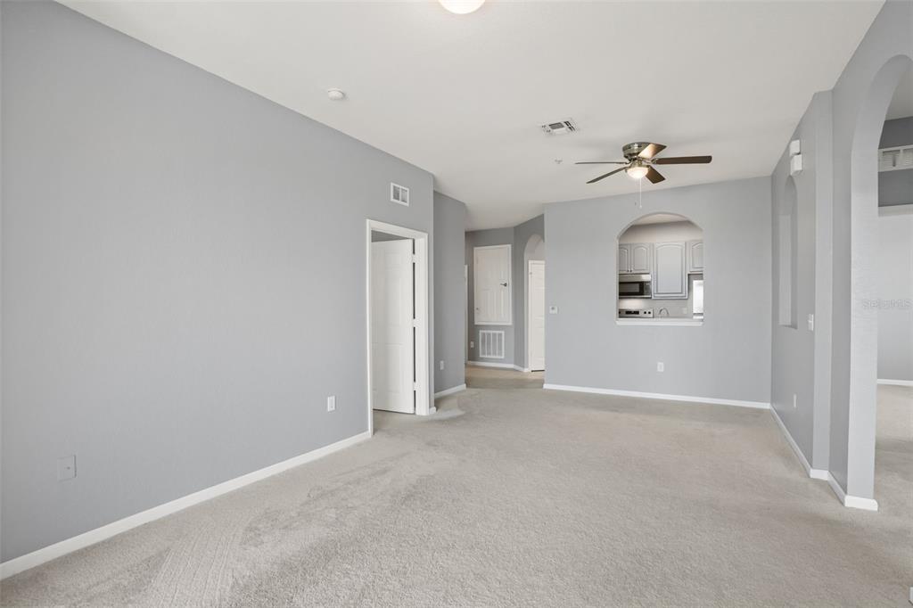 An empty living room with gray walls, beige carpeting, and a ceiling fan — 8775 SARTORI STREET UNIT 303, ORLANDO, FL