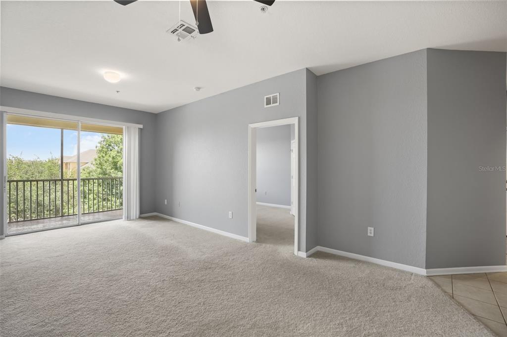A carpeted living room features gray walls, a ceiling fan, and a sliding glass balcony door — 8775 SARTORI STREET UNIT 303, ORLANDO, FL