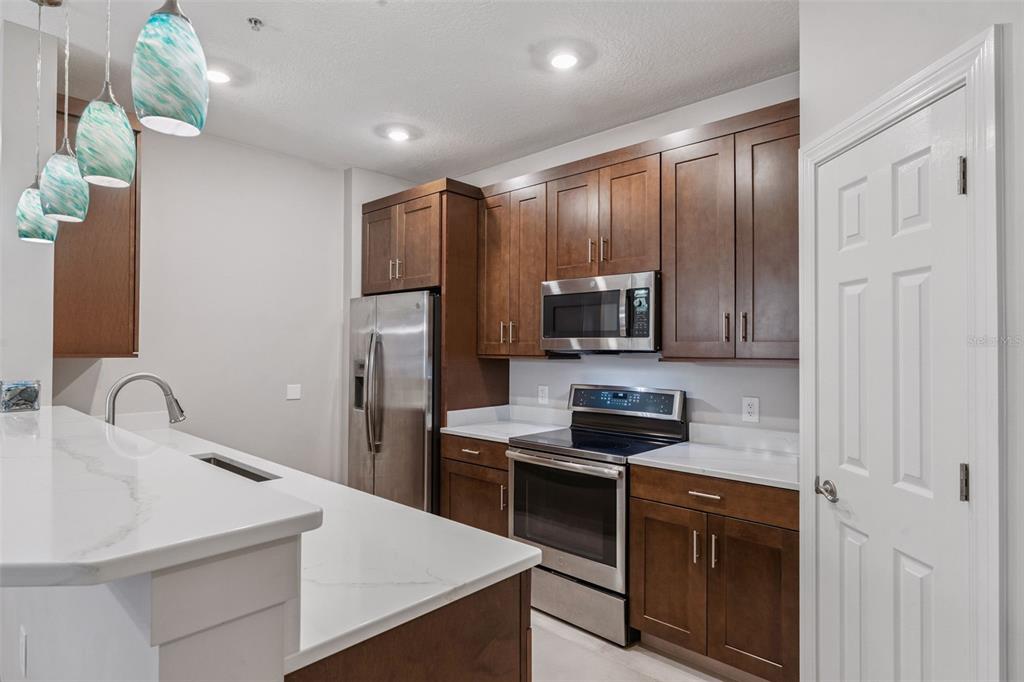 A kitchen features dark wood cabinets, stainless steel appliances, and a white quartz breakfast bar — 2484 SAN TECLA STREET UNIT 105, ORLANDO, FL