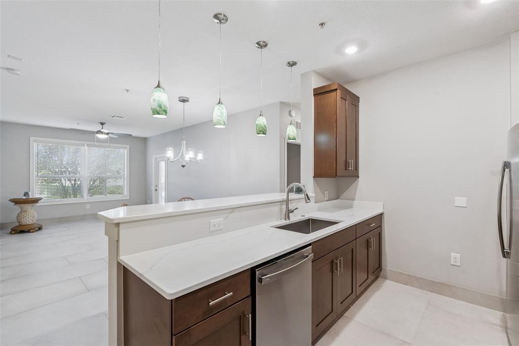 A kitchen with dark wood cabinets, white countertops, and pendant lighting overlooking an open living area — 2484 SAN TECLA STREET UNIT 105, ORLANDO, FL