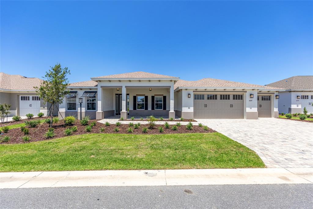A single-story house with a beige stucco exterior, a paved driveway, and a three-car garage — 10247 SW 82ND PLACE ROAD, OCALA, FL