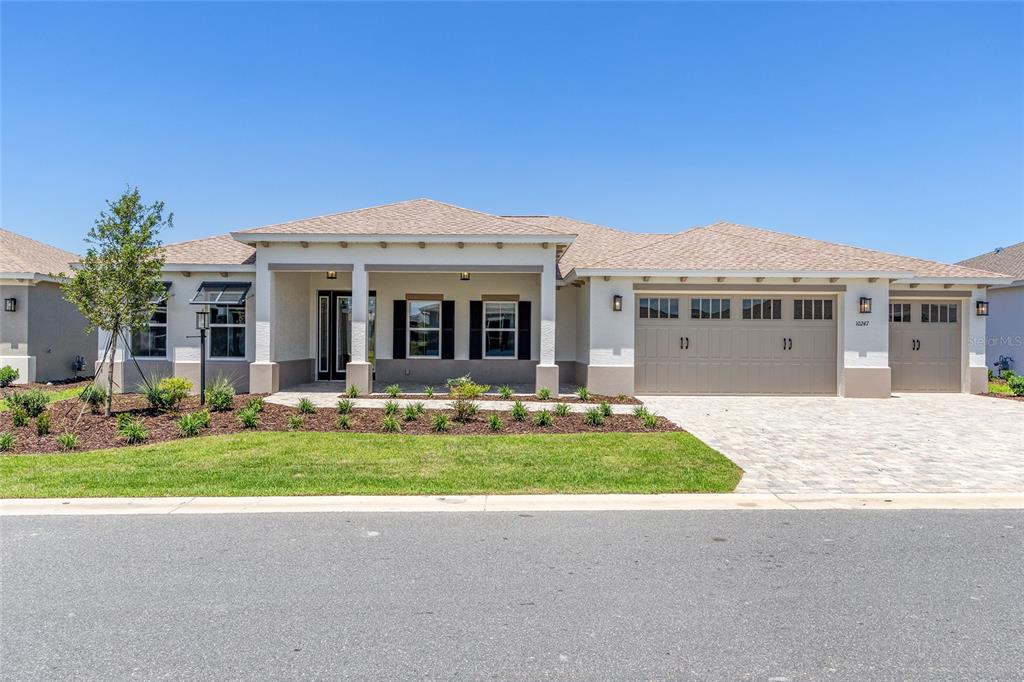 A single-story house with a tan stucco exterior, a three-car garage, and a covered entryway — 10247 SW 82ND PLACE ROAD, OCALA, FL