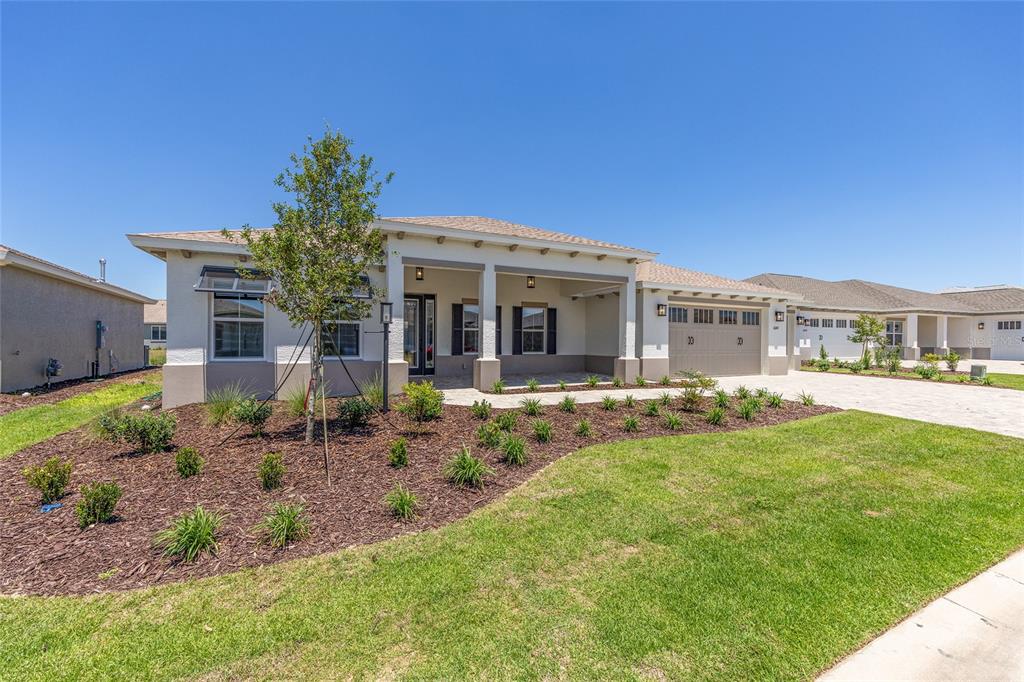 A single-story house with a covered front porch, a two-car garage, and landscaped mulch beds — 10247 SW 82ND PLACE ROAD, OCALA, FL