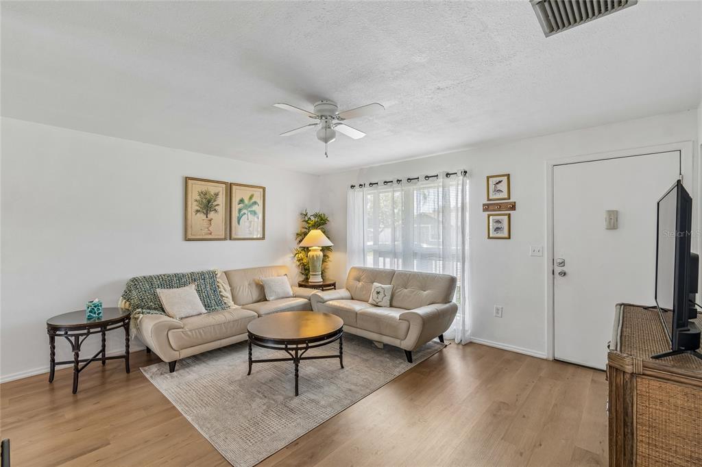 A living room features light wood flooring, two beige sofas, a round coffee table, and a rug — 3506 MURROW STREET, NEW PORT RICHEY, FL