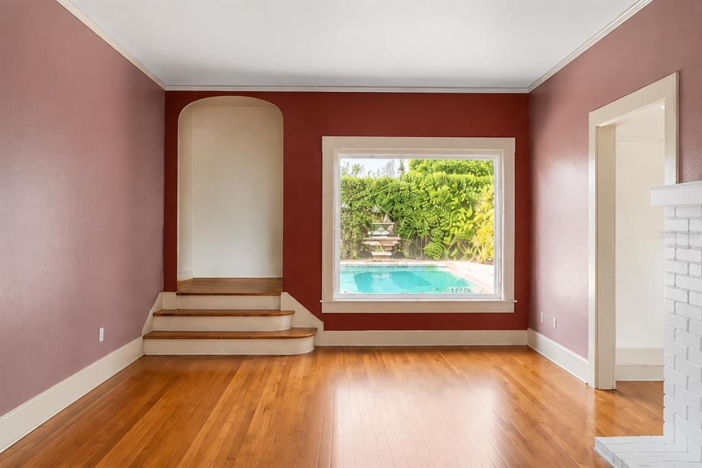 A room with hardwood floors, mauve and red walls, a fireplace, and a pool view — 4535 9TH AVENUE N, ST PETERSBURG, FL