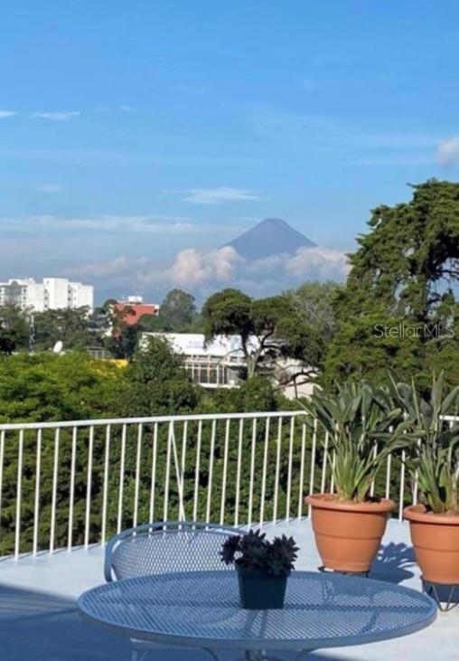 A balcony with a metal table and potted plants overlooks trees and a distant volcano — 15-25 AVE REFORMA, GUATEMALA CITY, OC