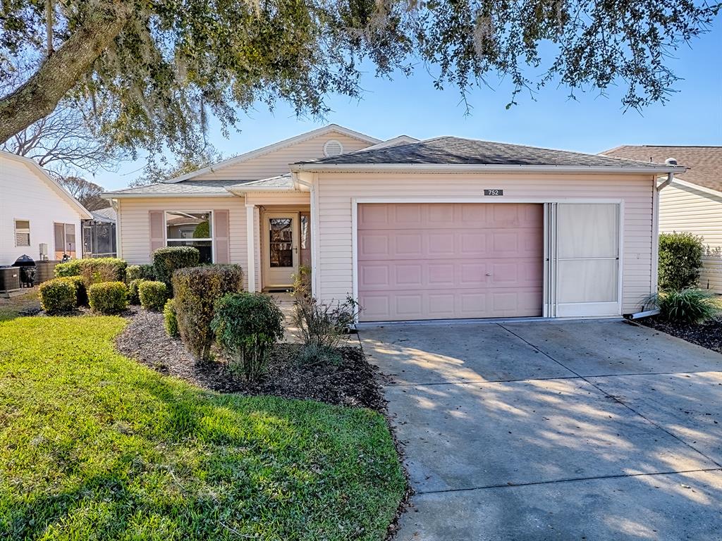 A single-story house with light siding, a two-car garage, and a landscaped front yard — 752 OLD OAKS LANE, LEESBURG, FL