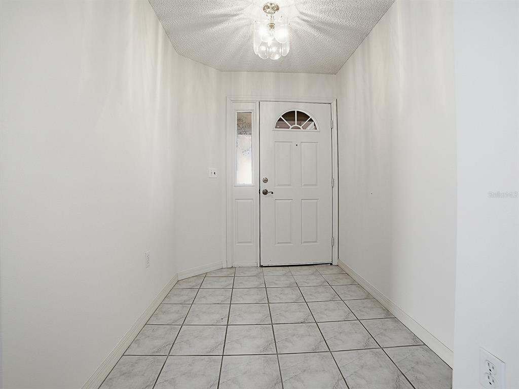 A tiled entryway features white walls, a textured ceiling, and a white front door — 752 OLD OAKS LANE, LEESBURG, FL