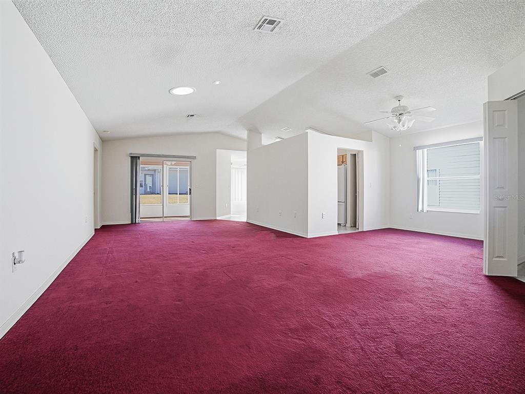 A spacious, empty living room features deep red carpeting, white walls, and a vaulted ceiling — 752 OLD OAKS LANE, LEESBURG, FL
