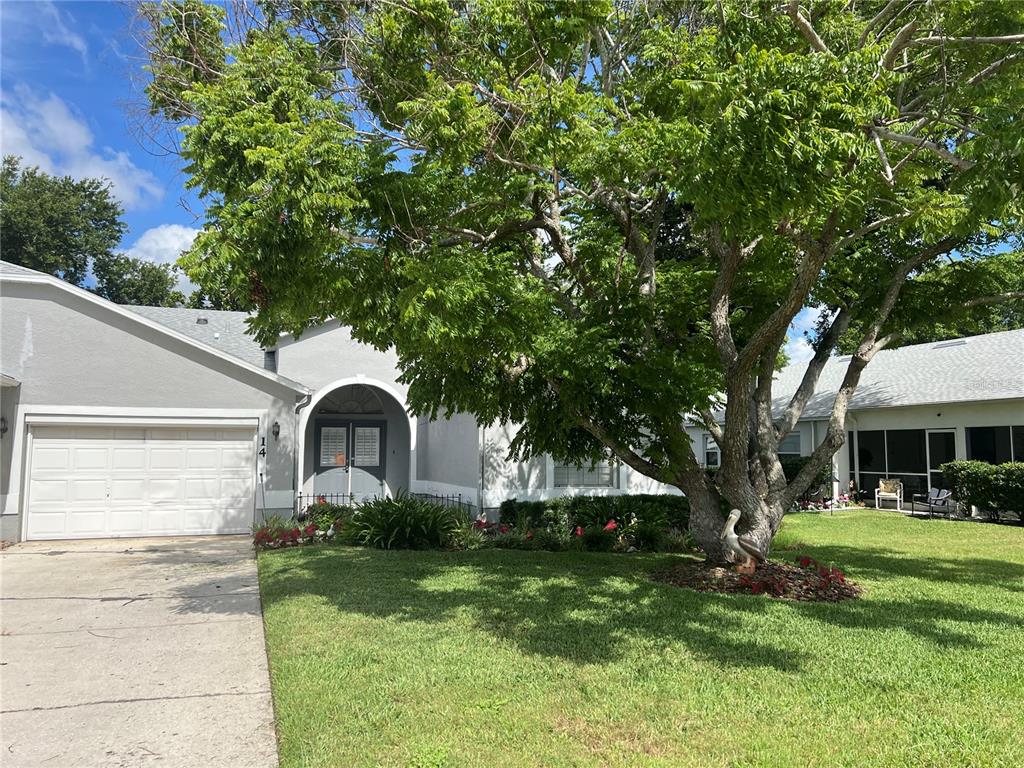 A single-story house with a white garage, arched entryway, and a large tree in front — 6381 EGRET DRIVE UNIT 14, LAKELAND, FL