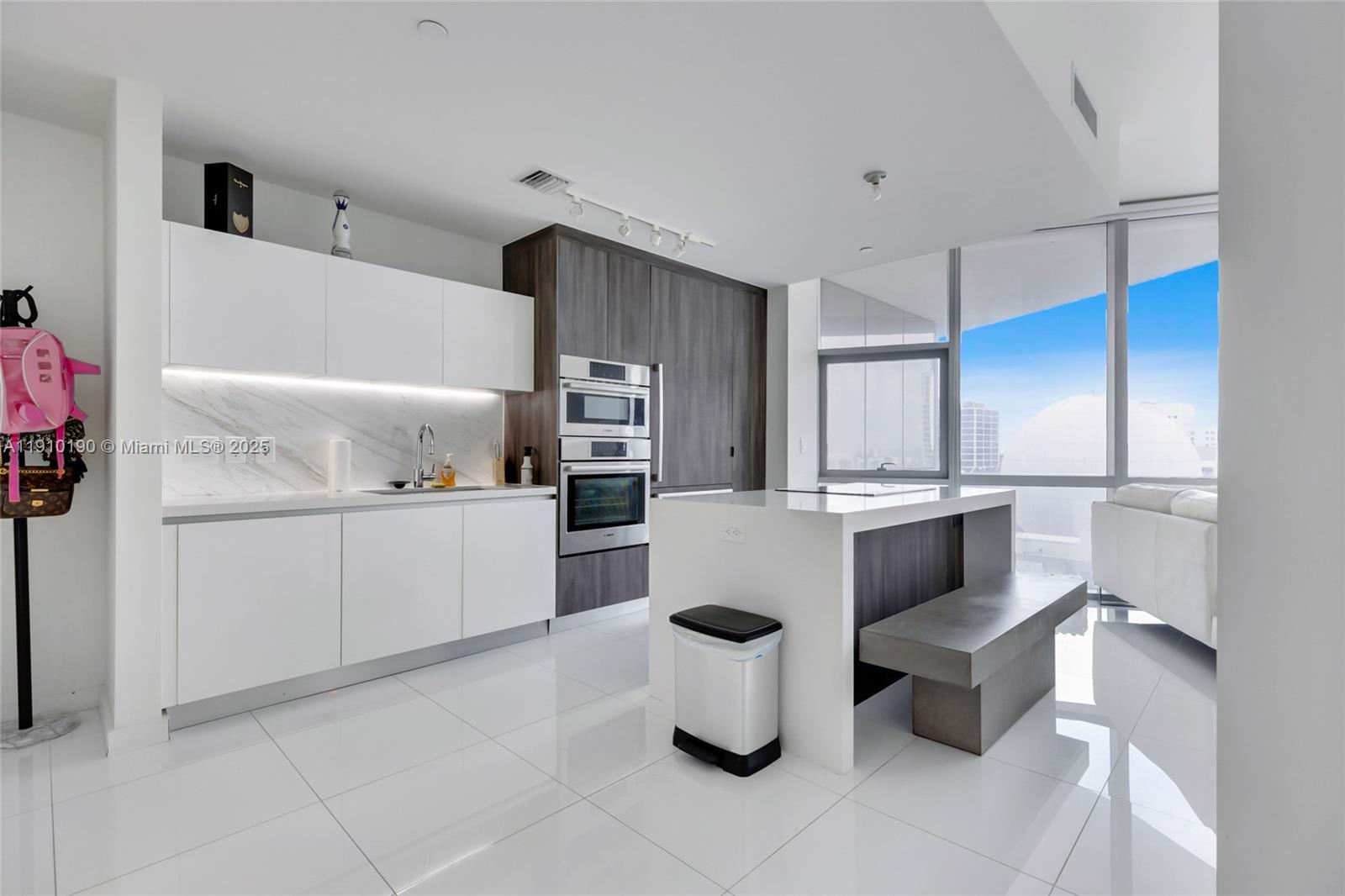 A modern kitchen features white cabinetry, a marble backsplash, stainless steel appliances, and a central island — 851 NE 1st Ave # 1202, Miami FL 33132, MIAMI, FL