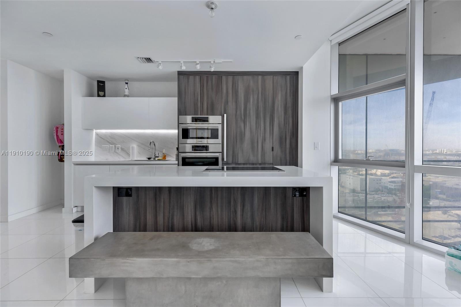 A modern kitchen features a white island with a concrete bench and dark cabinetry — 851 NE 1st Ave # 1202, Miami FL 33132, MIAMI, FL