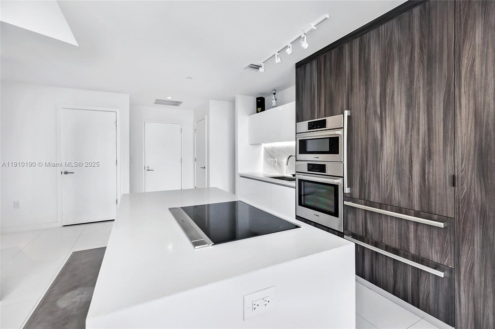 A modern kitchen features a white island with a cooktop and dark wood cabinetry — 851 NE 1st Ave # 1202, Miami FL 33132, MIAMI, FL