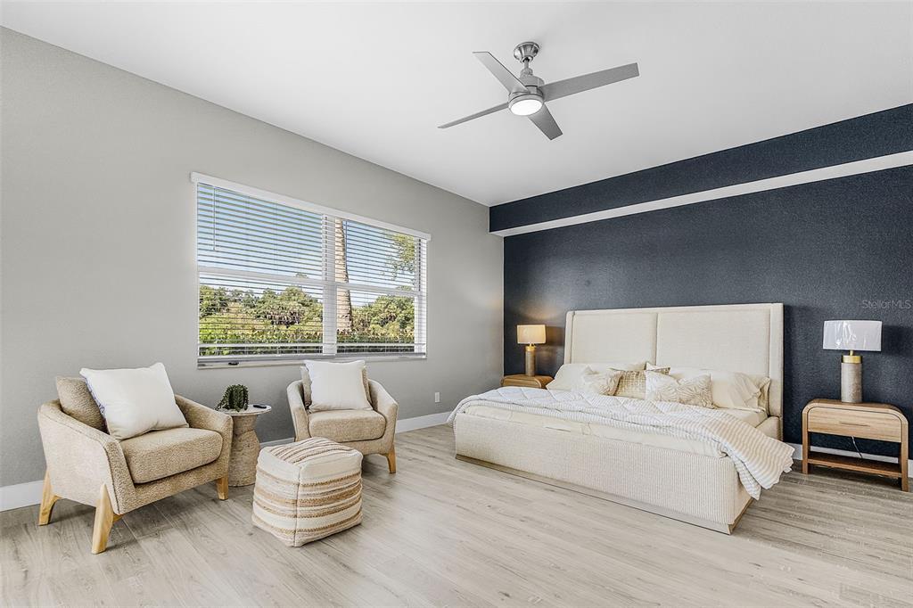 A bedroom features a dark accent wall, a light-colored bed, two armchairs, and a ceiling fan — 14081 BLACK BEAUTY DRIVE UNIT 1111, PUNTA GORDA, FL