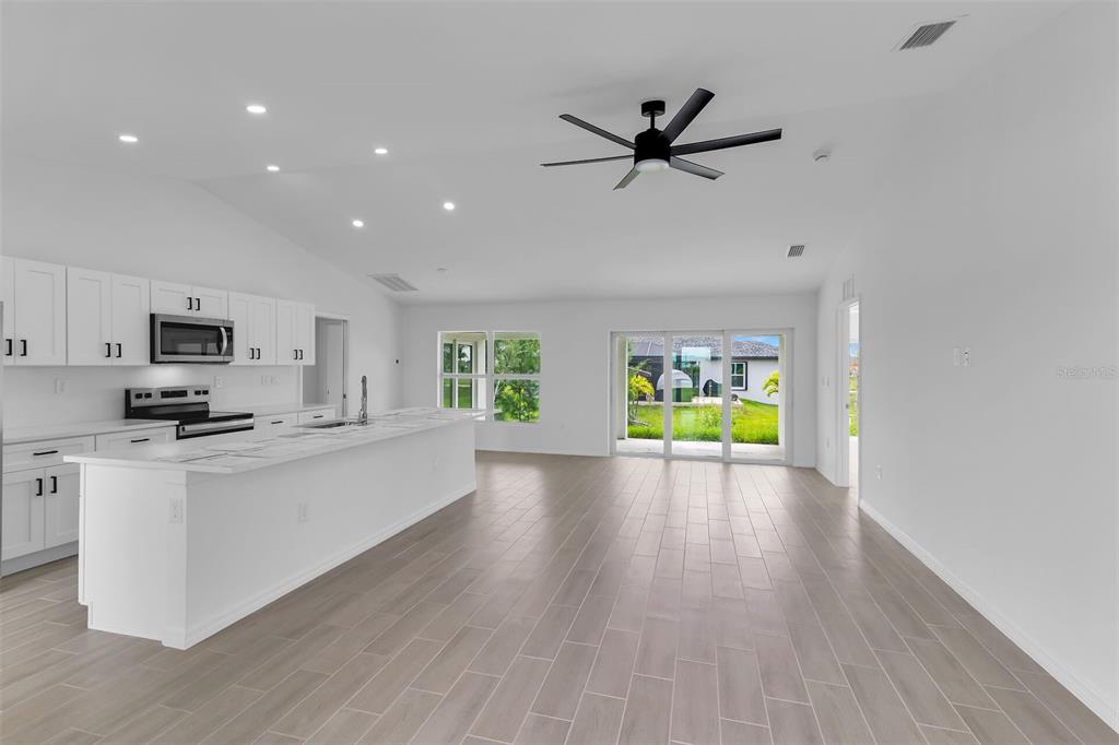 A bright, open-concept kitchen and living area with white cabinetry, an island, and tile flooring — 2221 NW 43RD AVENUE, CAPE CORAL, FL