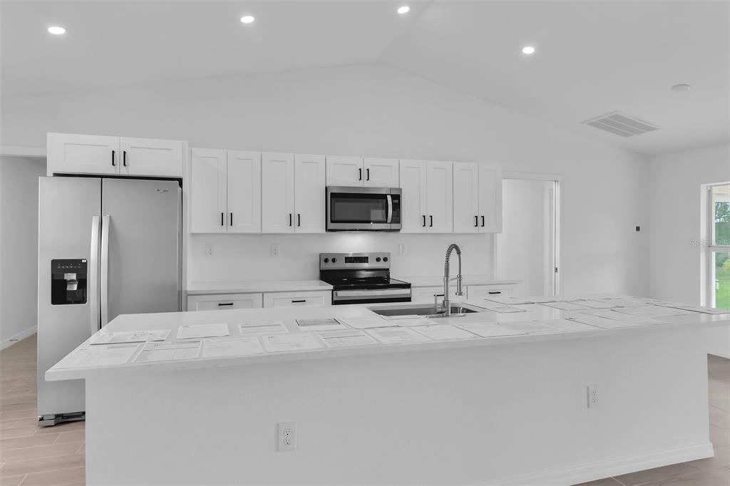A modern kitchen features white cabinets, stainless steel appliances, and a large central island — 2221 NW 43RD AVENUE, CAPE CORAL, FL