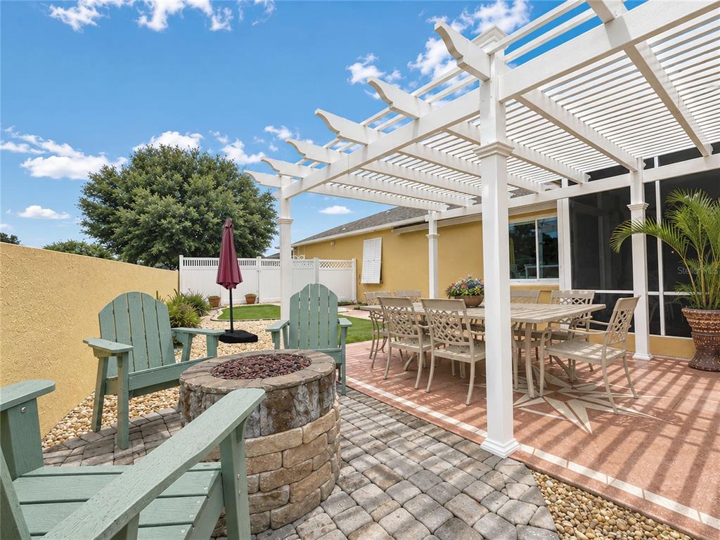 A backyard patio features a pergola, a stone fire pit, and outdoor dining furniture — 853 WINCHESTER COURT, THE VILLAGES, FL