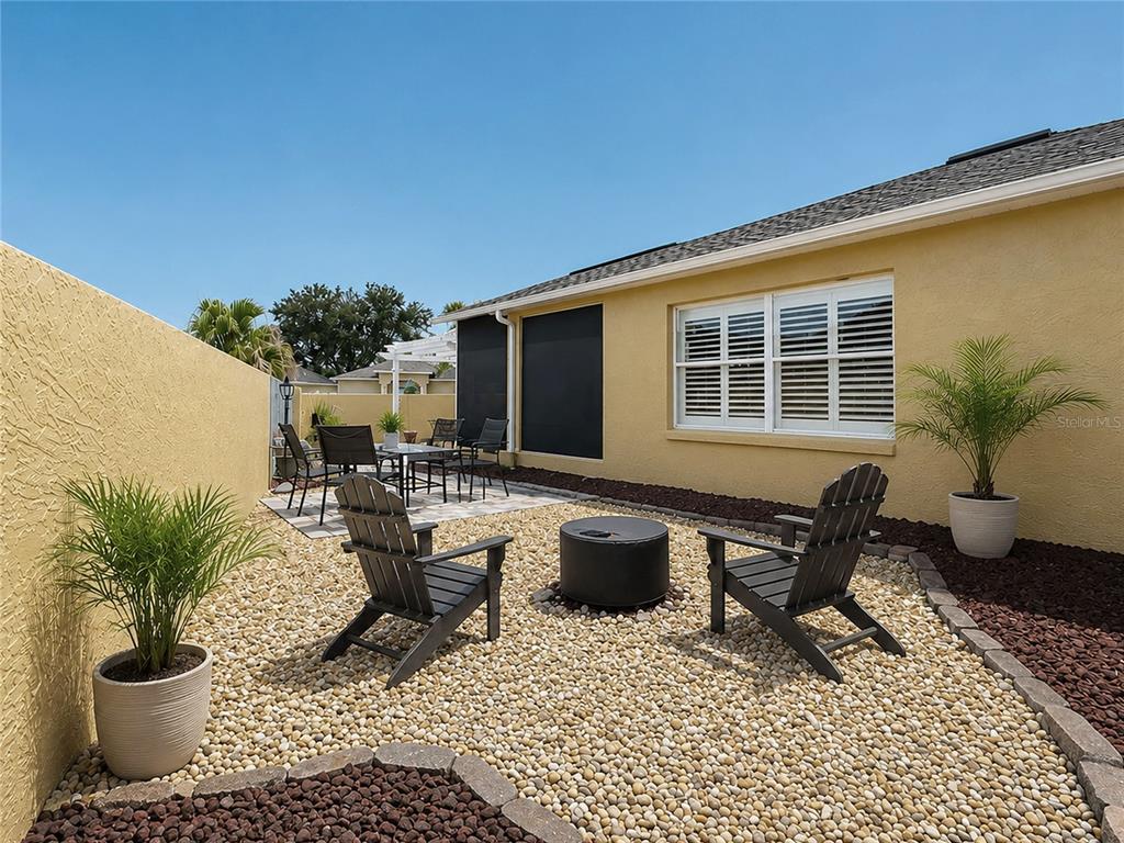 A backyard patio features a gravel ground cover, two Adirondack chairs, and a fire pit — 853 WINCHESTER COURT, THE VILLAGES, FL