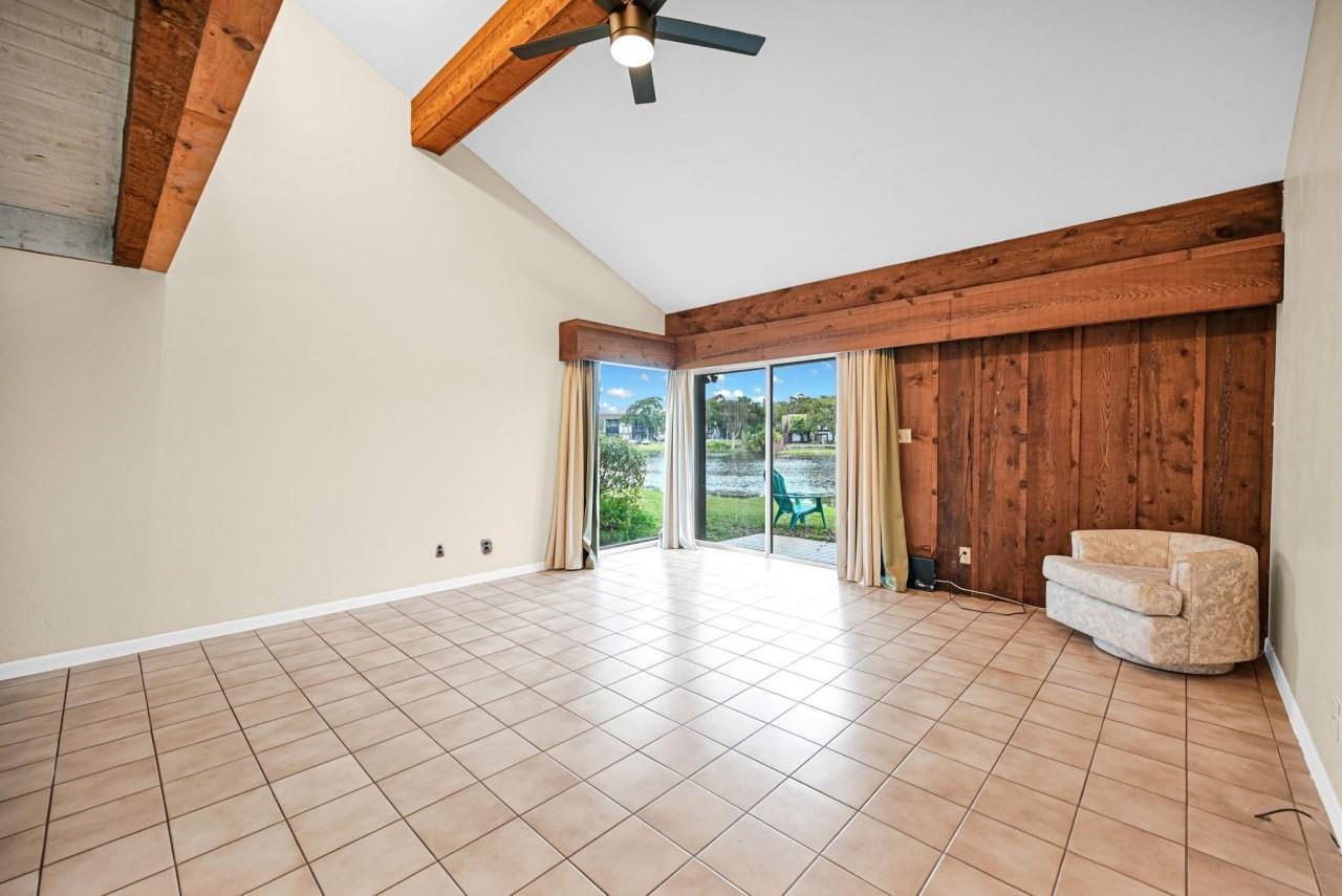 A living room features vaulted ceilings with exposed wood beams, tile flooring, and sliding glass doors — 3465 Spring Bluff Place # 18, Lauderhill FL 33319, LAUDERHILL, FL