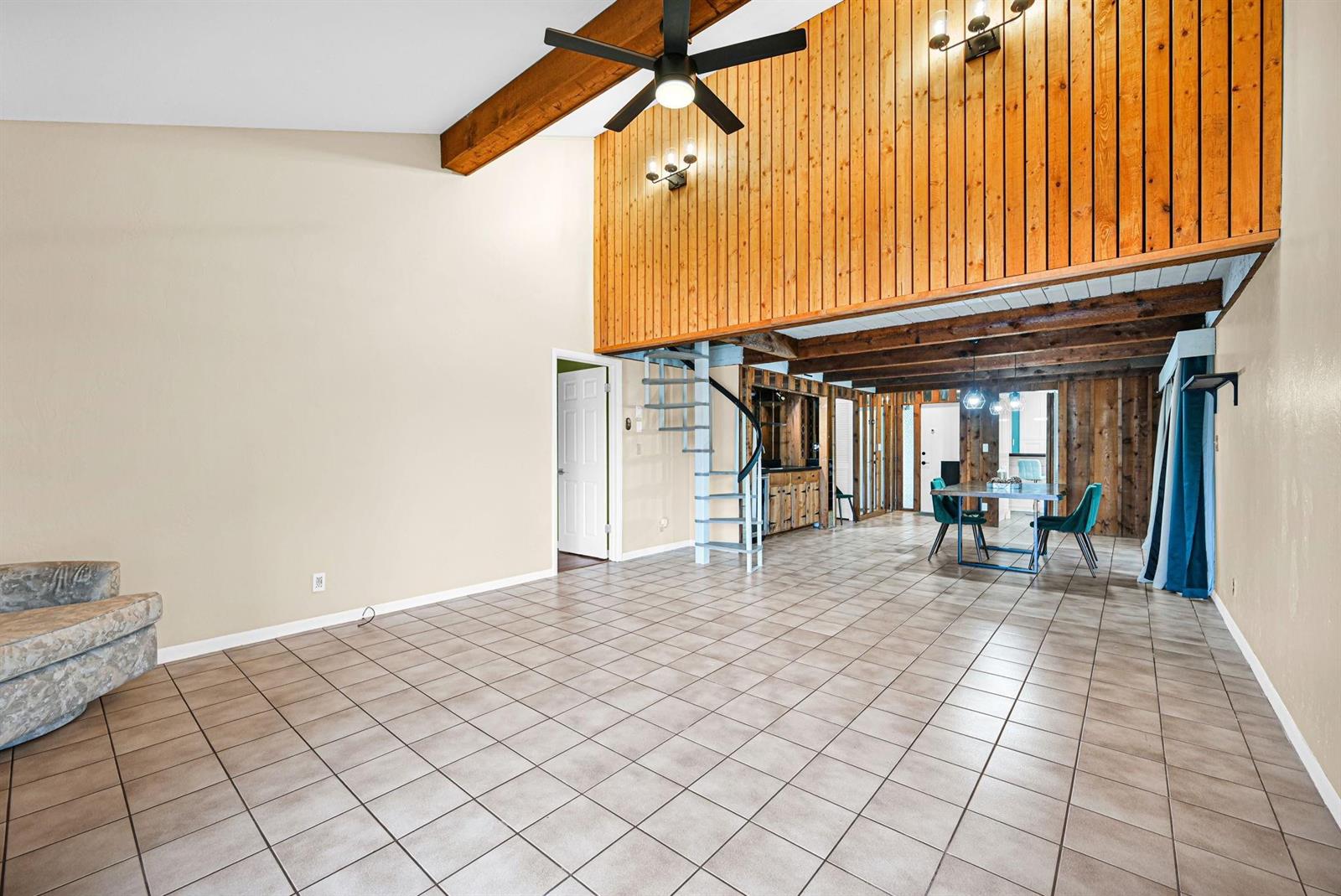 A spacious living and dining area features tile flooring, a spiral staircase, and wood-paneled walls — 3465 Spring Bluff Place # 18, Lauderhill FL 33319, LAUDERHILL, FL