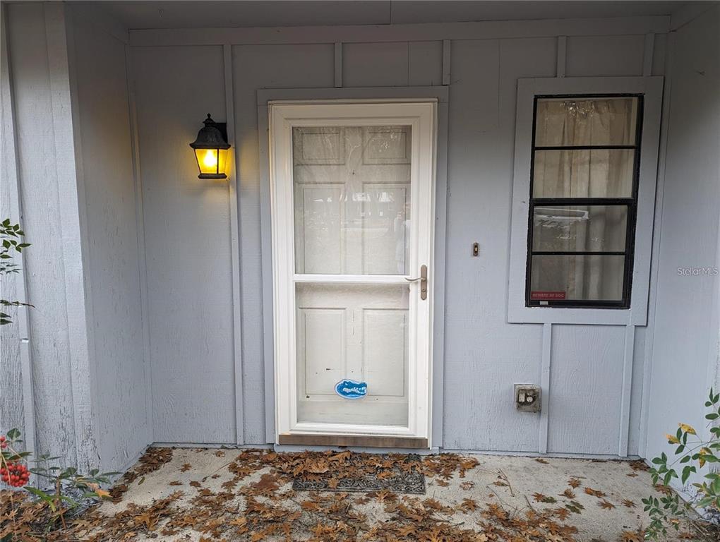 A gray exterior wall features a white storm door, a window, and a wall lamp — 721 SW 127TH STREET, NEWBERRY, FL