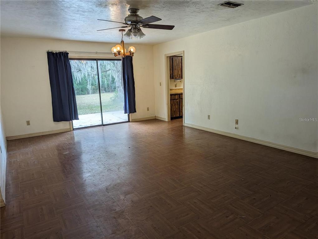 An empty room features parquet flooring, a ceiling fan, a chandelier, and sliding glass doors — 721 SW 127TH STREET, NEWBERRY, FL