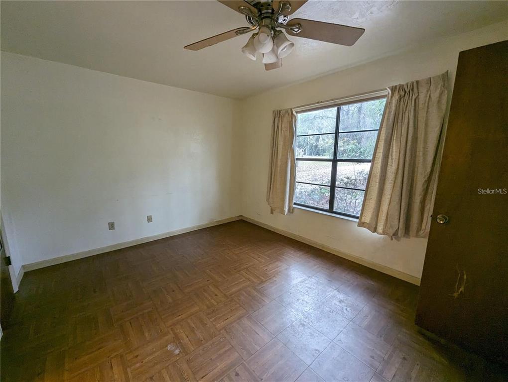 An empty bedroom features parquet flooring, a ceiling fan, and a window with curtains — 721 SW 127TH STREET, NEWBERRY, FL