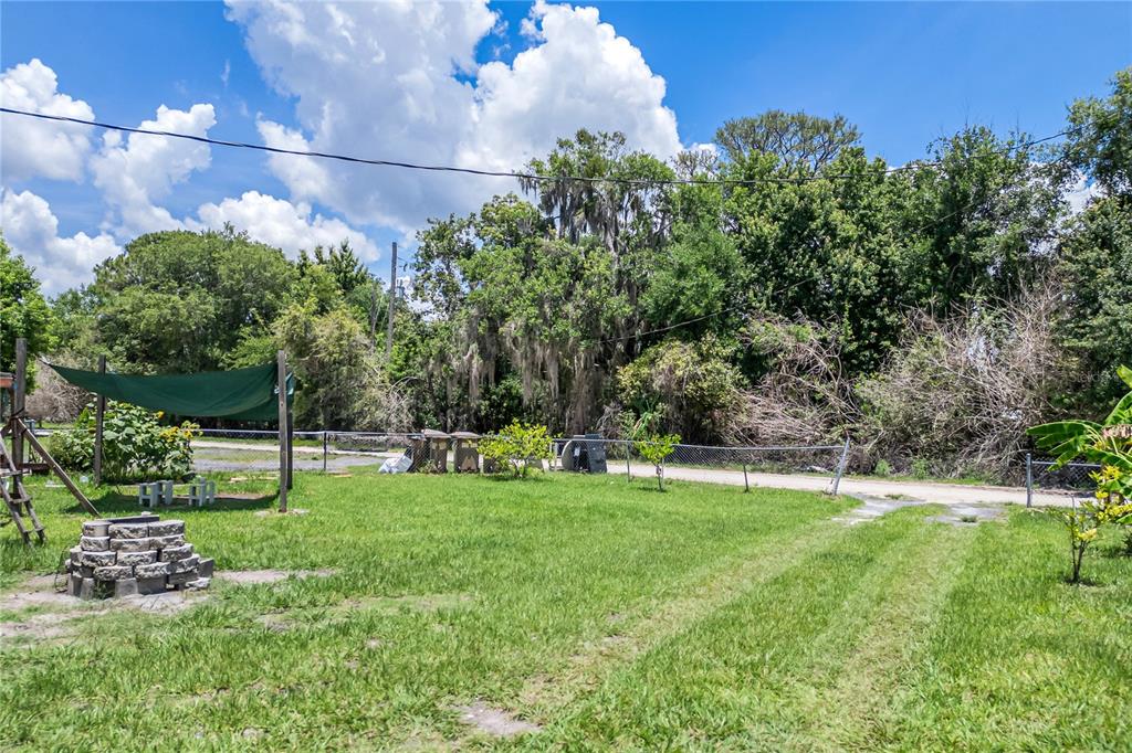 A grassy backyard features a stone fire pit, a green shade canopy, and a chain-link fence — 4960 YUKON STREET, ST CLOUD, FL
