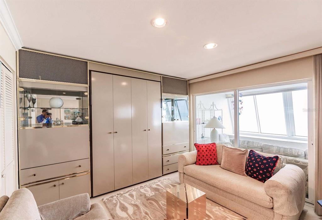 A living room features a large wall unit, a beige sofa, and a sunroom beyond — 1055 W PEPPERTREE DRIVE UNIT 802AA, SARASOTA, FL