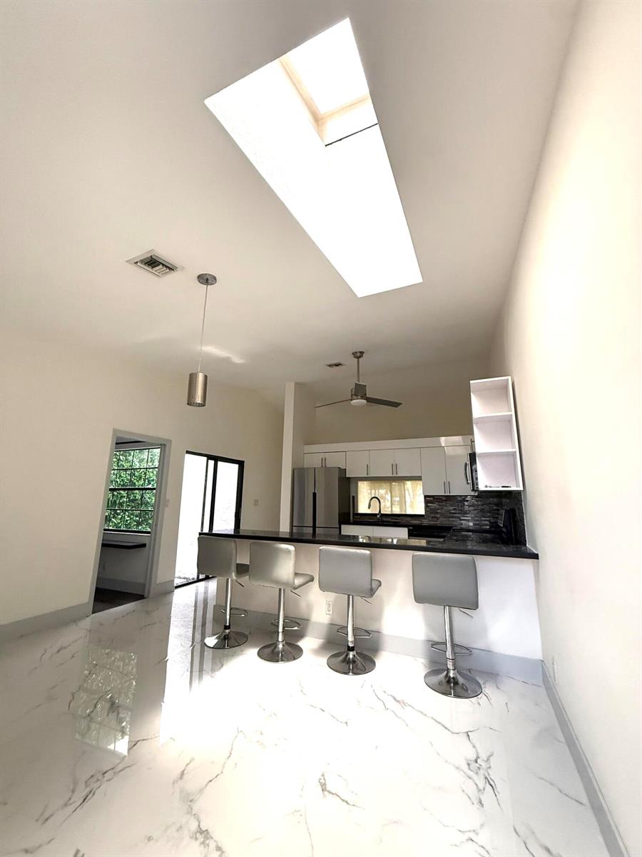 A kitchen with a breakfast bar, white cabinets, and a skylight over a tiled floor — 5161 NW 11th Lane, Deerfield Beach FL 33064, DEERFIELD BEACH, FL