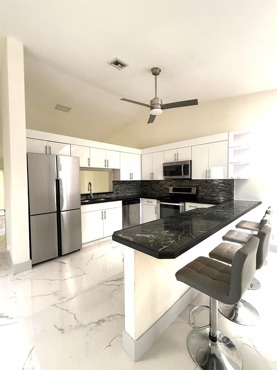 A modern kitchen features white cabinets, stainless steel appliances, dark countertops, and white marble flooring — 5161 NW 11th Lane, Deerfield Beach FL 33064, DEERFIELD BEACH, FL