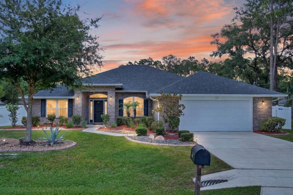 A single-story brick house with a two-car garage and a landscaped front yard at sunset — 24 LINCOLN LANE, PALM COAST, FL
