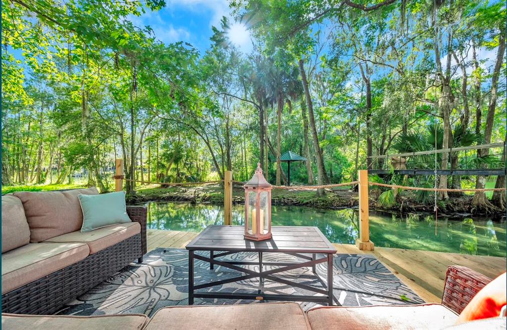 A wooden deck with outdoor furniture overlooks a calm river surrounded by lush green trees — 11426 SW HENDRIX DRIVE, DUNNELLON, FL