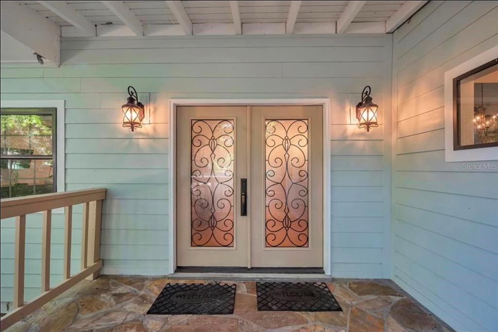 A front porch with light blue siding, stone flooring, and double doors with decorative glass inserts — 11426 SW HENDRIX DRIVE, DUNNELLON, FL