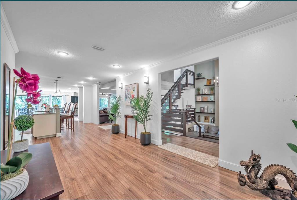 A hallway with wood-look flooring leads to an open kitchen and a staircase with shelving — 11426 SW HENDRIX DRIVE, DUNNELLON, FL