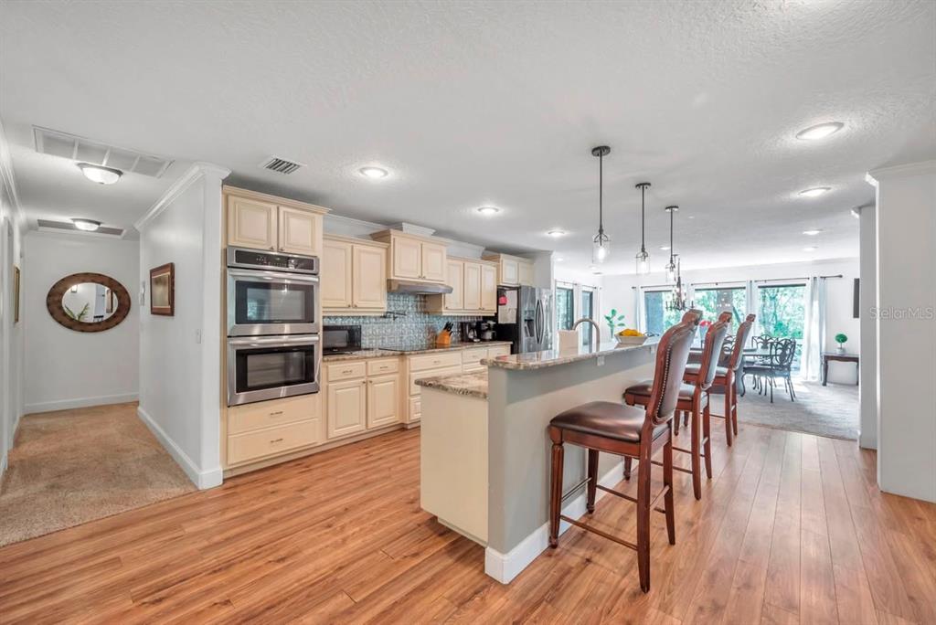 A kitchen features light-colored cabinets, stainless steel double ovens, a breakfast bar, and wood flooring — 11426 SW HENDRIX DRIVE, DUNNELLON, FL