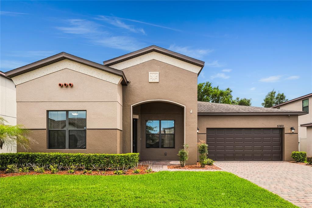 A single-story house with a brown stucco exterior, a two-car garage, and a manicured lawn — 5160 SASSARI AVENUE, ST CLOUD, FL