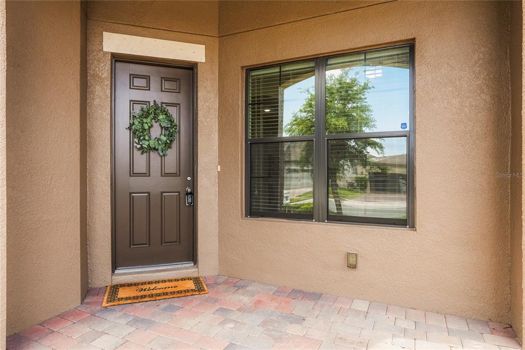A brown front door with a wreath and a welcome mat sits on a porch — 5160 SASSARI AVENUE, ST CLOUD, FL