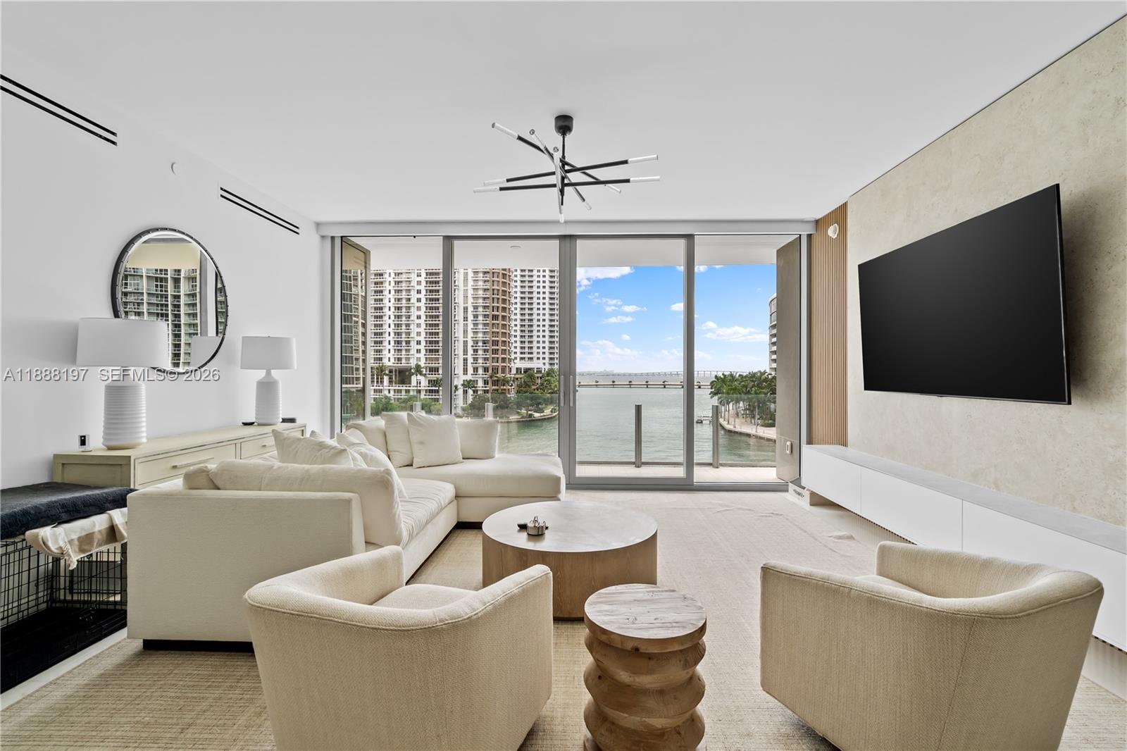 A modern living room features a white sectional, two armchairs, and a waterfront balcony view — 300 Biscayne Blvd Way # 1103, Miami FL 33131, MIAMI, FL