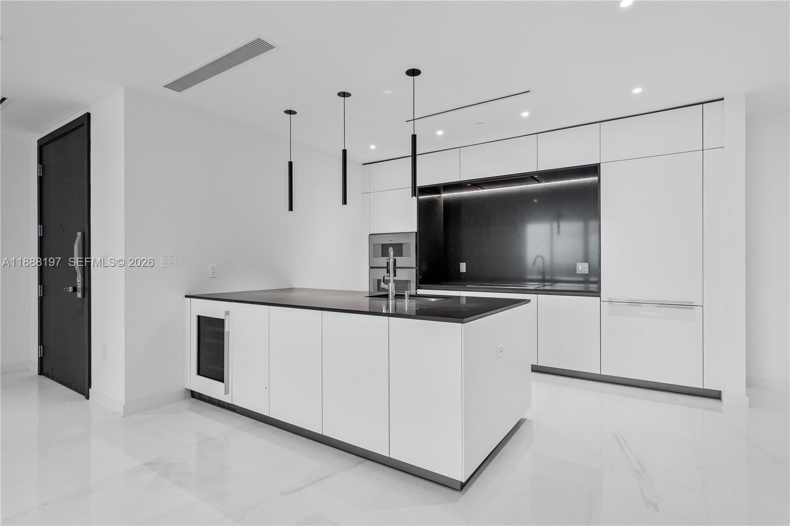 A modern kitchen features white cabinetry, a black island countertop, and minimalist pendant lighting — 300 Biscayne Blvd Way # 1103, Miami FL 33131, MIAMI, FL