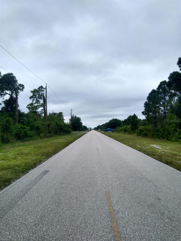 A paved road stretches into the distance between grassy shoulders and lines of trees — 12952 FORESMAN BOULEVARD, PORT CHARLOTTE, FL