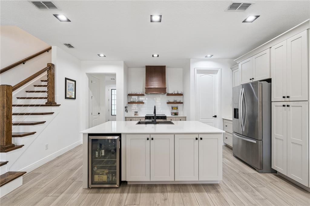 A modern kitchen features a central island, white cabinetry, stainless steel appliances, and wood flooring — 15524 HONEYBELL DRIVE, WINTER GARDEN, FL