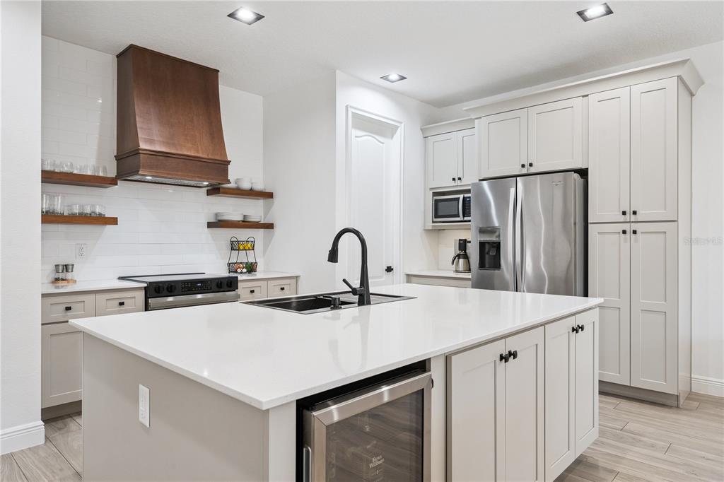 A modern kitchen features a white island, stainless steel appliances, and wood floating shelves — 15524 HONEYBELL DRIVE, WINTER GARDEN, FL