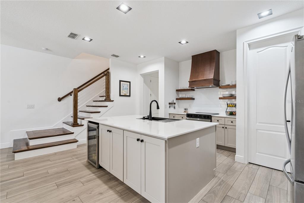 A modern kitchen features a white island, wooden range hood, and stairs with wood treads — 15524 HONEYBELL DRIVE, WINTER GARDEN, FL