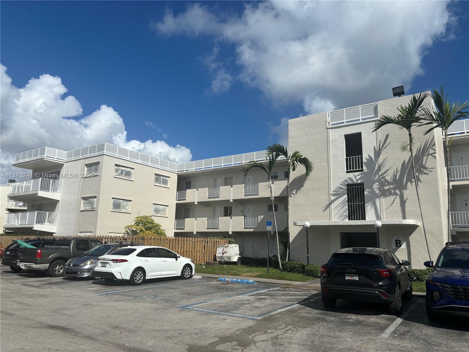 A multi-story apartment building with a parking lot and palm trees under a blue sky — 7701 SW 88th St # B224, Miami FL 33156, MIAMI, FL